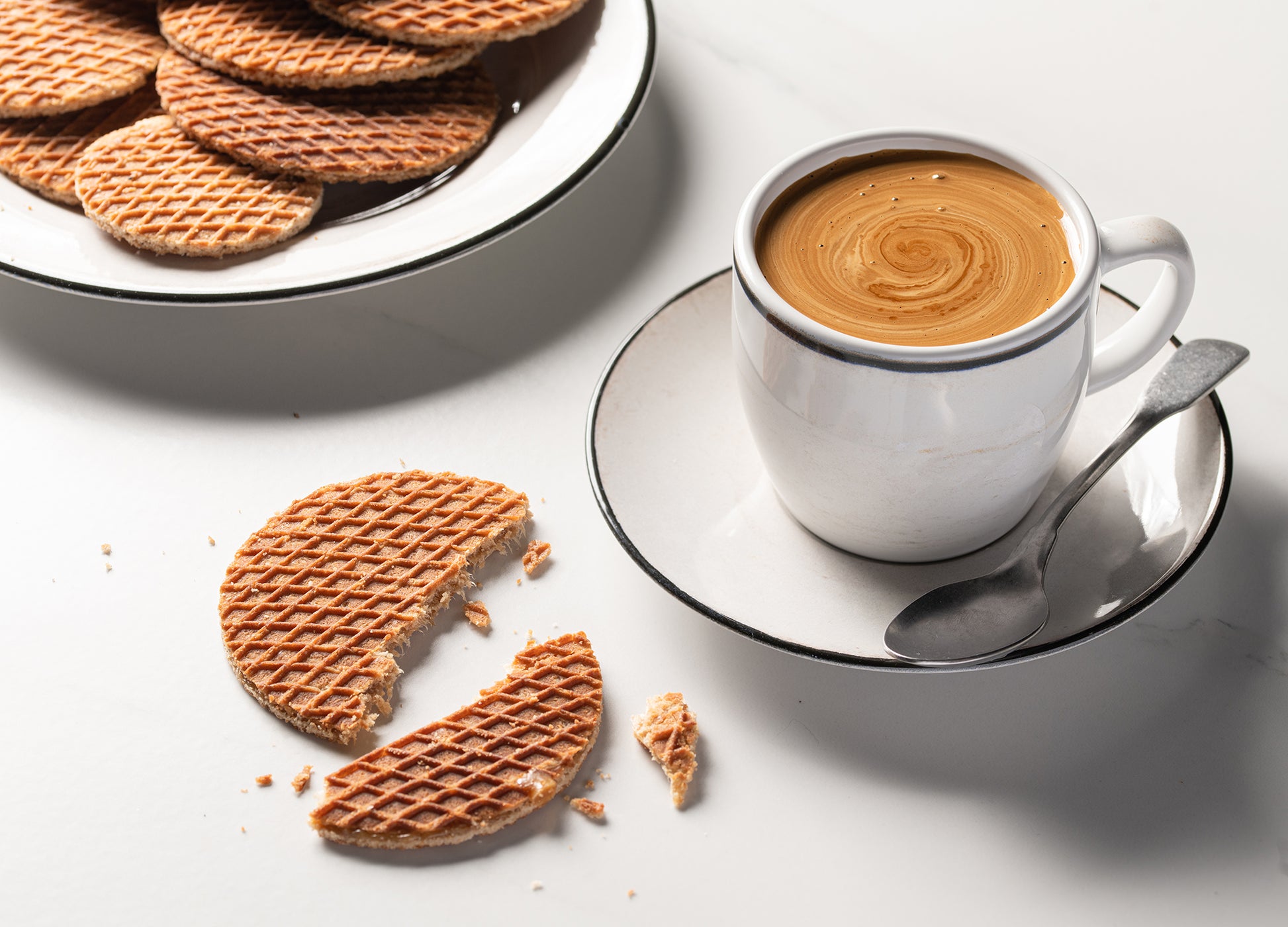 A cup of coffee and Wonderen Stroopwafels' Authentic Green Stroopwafel Tin Can with Refill on a white plate.